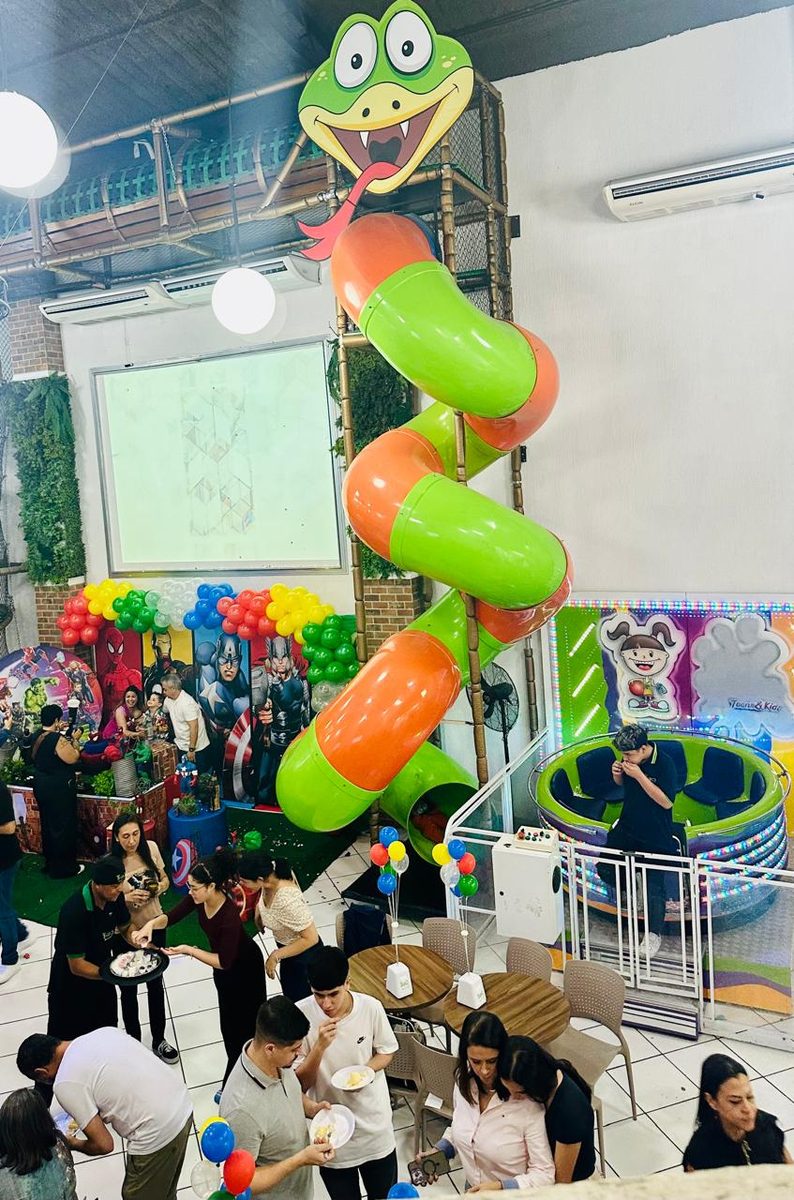 Salão da unidade Kids cheio em dia de festa, com o tobogã em espiral e as mesas ocupadas