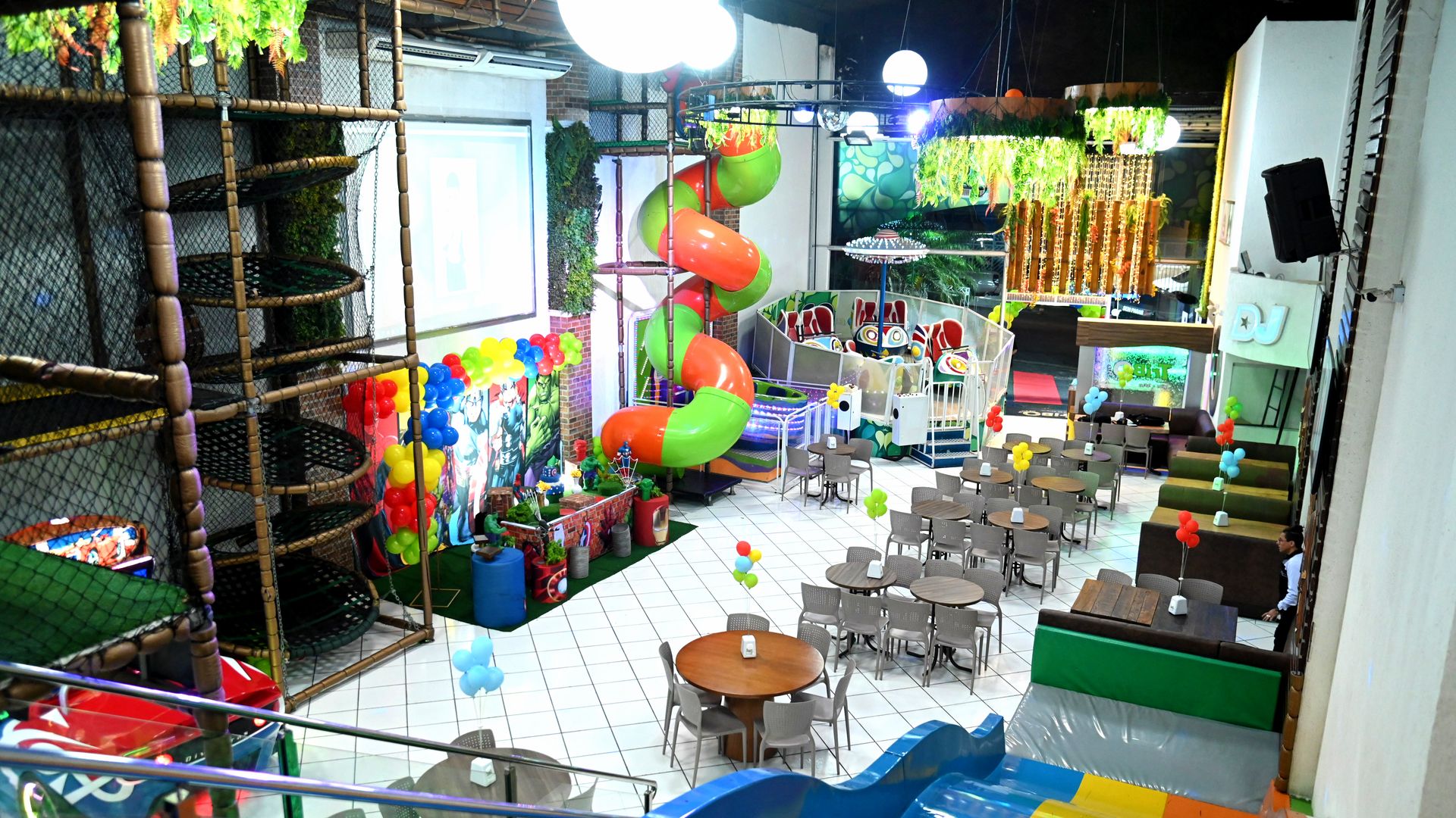 Salão da unidade Kids & Teens montado para uma festa, com brinquedão, tobogã e mesas postas