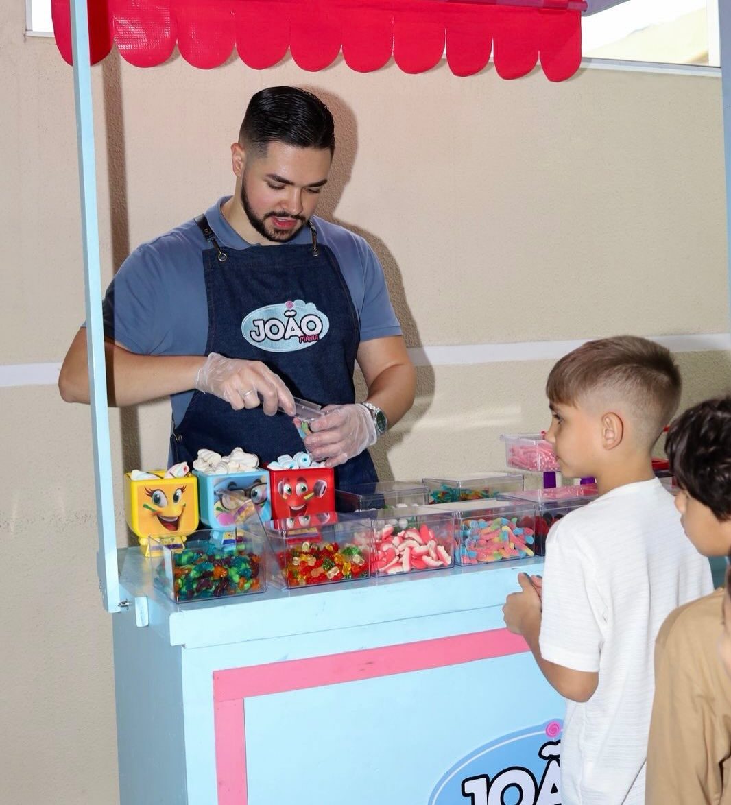 Atendente do João Mania montando um saquinho de balas para duas crianças