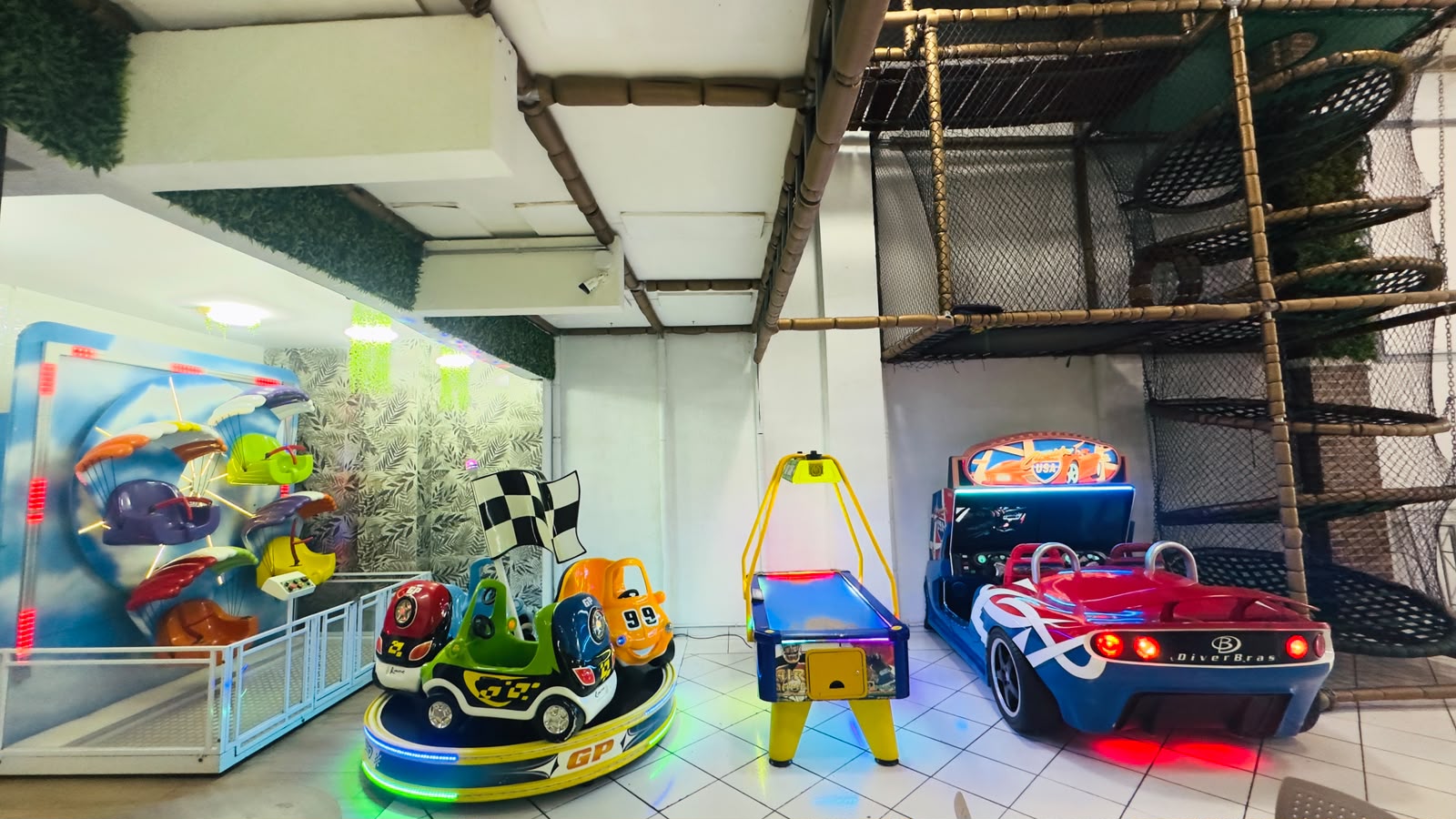 Área de atrações da Kids & Teens com simuladores de corrida, carrossel de carrinhos, aero hockey e brinquedo de paraquedas